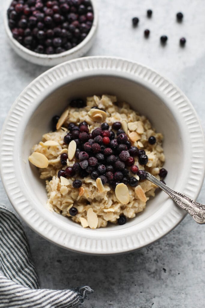 Overhead view oatmeal in white bowl topped with almonds and wild blueberries