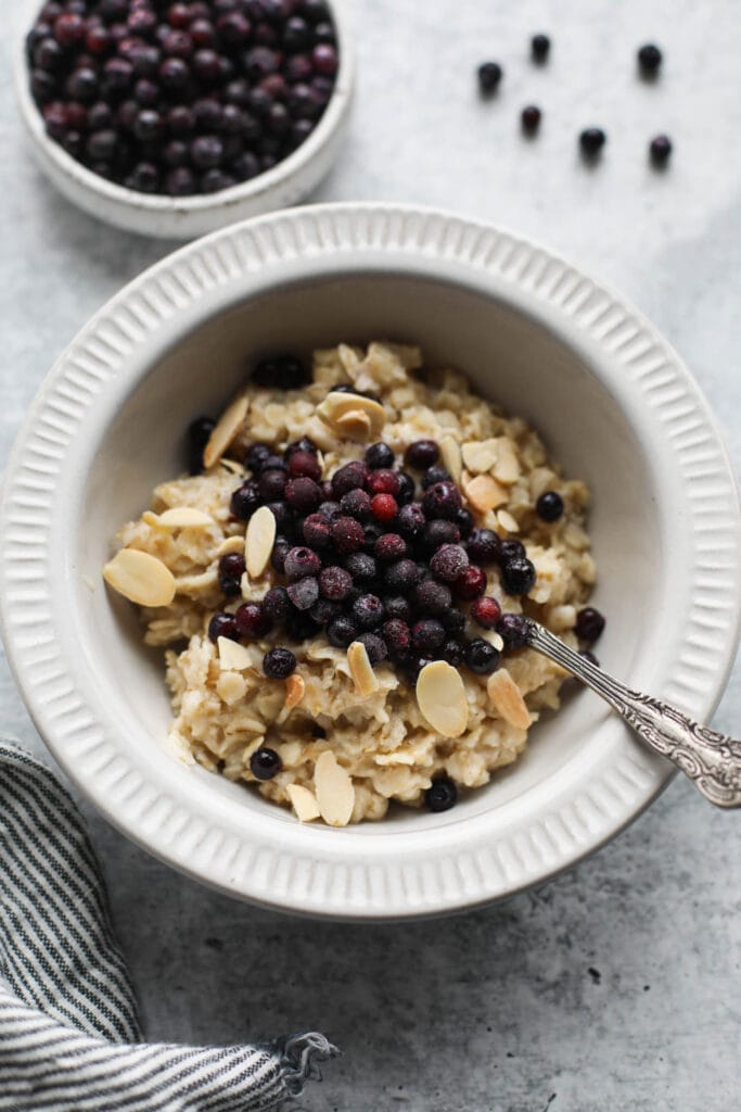 Overhead view of a bowl of oatmeal topped with wild blueberries and sliced almonds next to a bowl of blueberries in the background. 