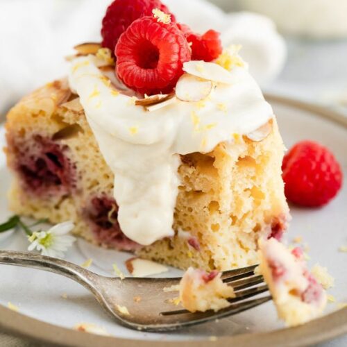 Slice of raspberry coffee cake on plate topped with lemon sour cream sauce.