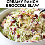 A forkful of creamy ranch broccoli slaw with dried cranberries being lifted up over a bowl full of slaw.