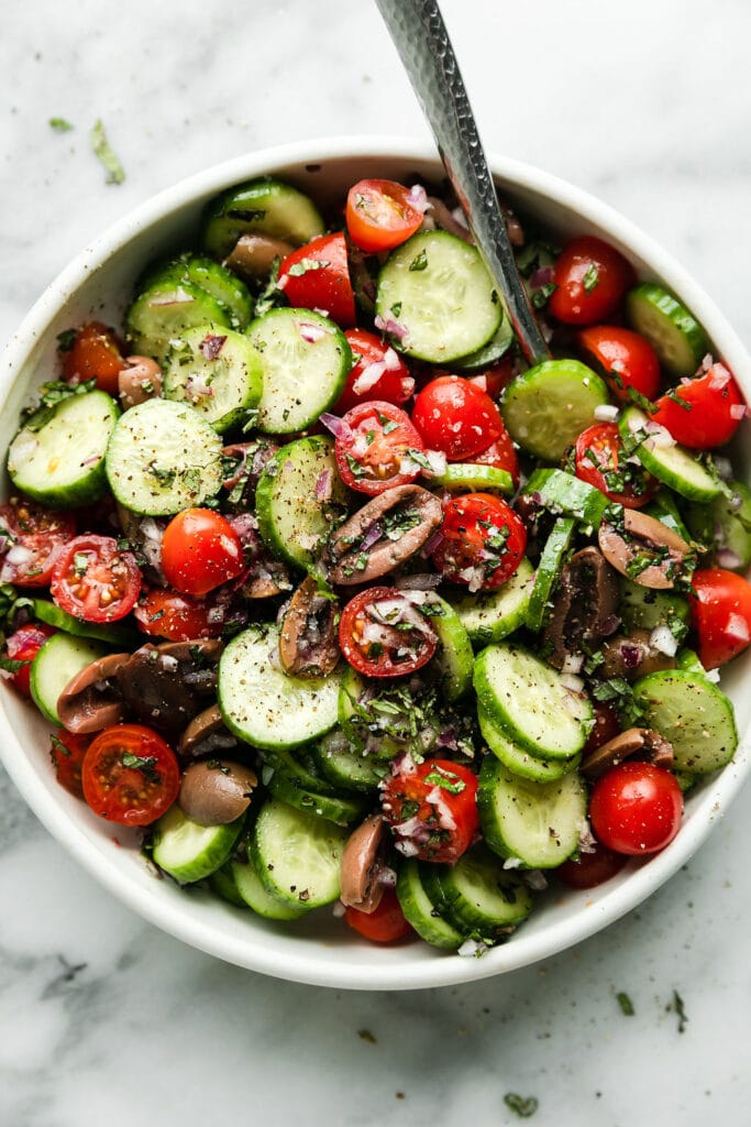 Cucumbers, tomatoes, and kalamata olives mixed into salad in white bowl