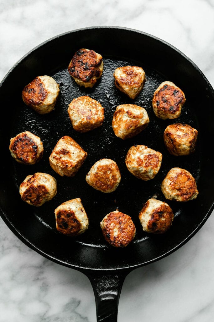Greek chicken meatballs browned in cast iron skillet. 