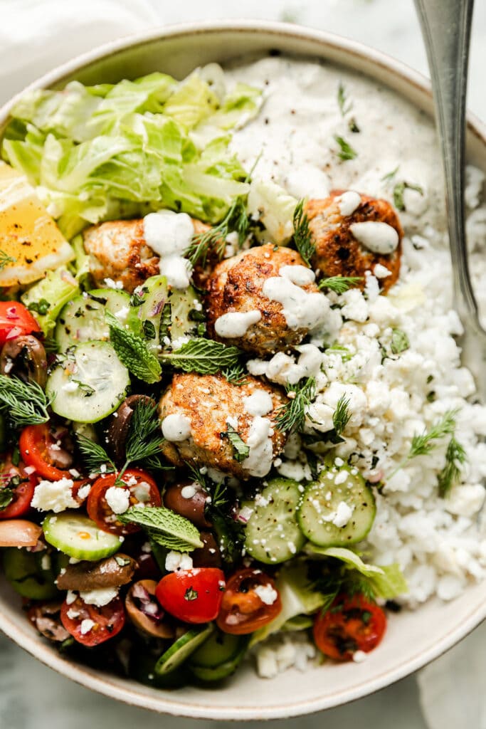 Close up view Greek salad bowl with chicken meatballs, topped with tzatziki sauce and fresh mint and dill leaves.