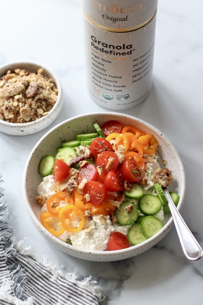 Stone bowl filled with cottage cheese topped with fresh cut veggie and Struesli, grain-free granola