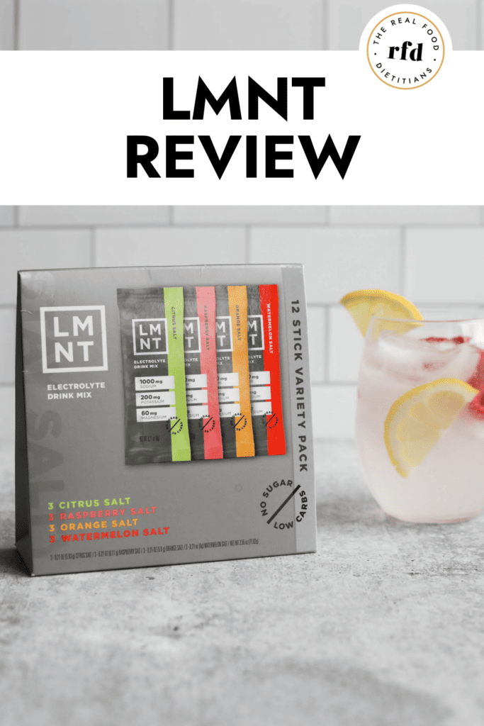 Sample pack of LMNT electrolyte drink mix on counter with small glass of water with lemon slices and fresh raspberries to the side