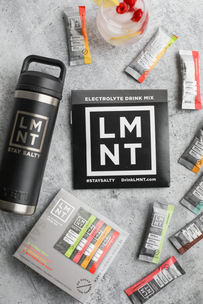 LMNT Electrolyte Drink Mix thermos, variety box, and individual stick laid out on a table. 