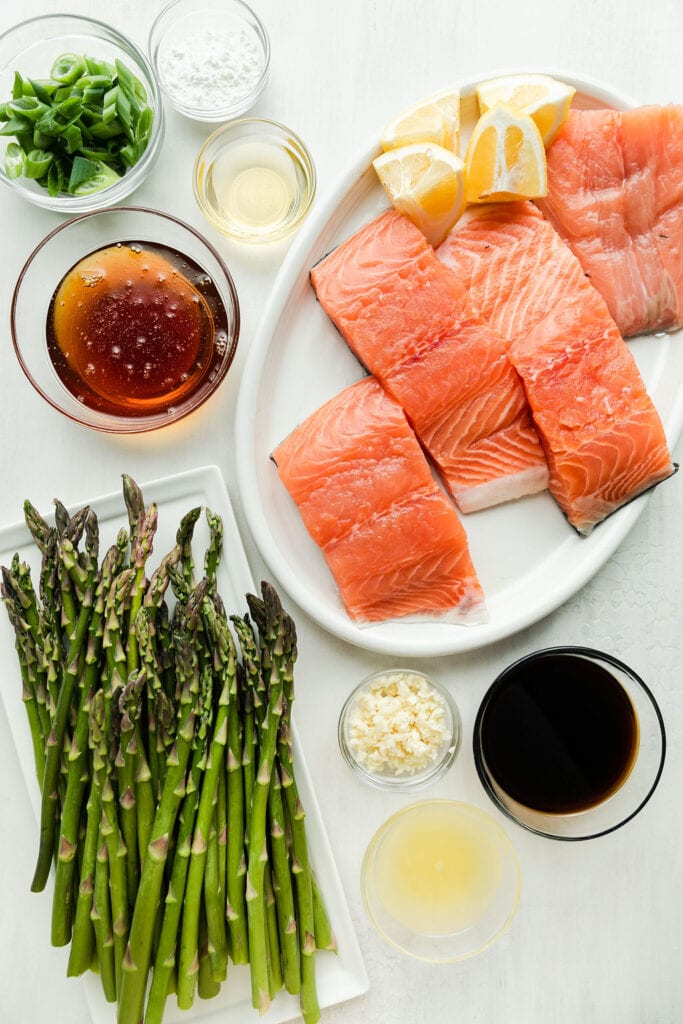 Overhead view all ingredients for honey glazed salmon with asparagus on plates and in bowls.