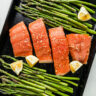 Overhead view sheet pan filled with raw salmon coated in honey glaze with fresh asparagus on both sides.