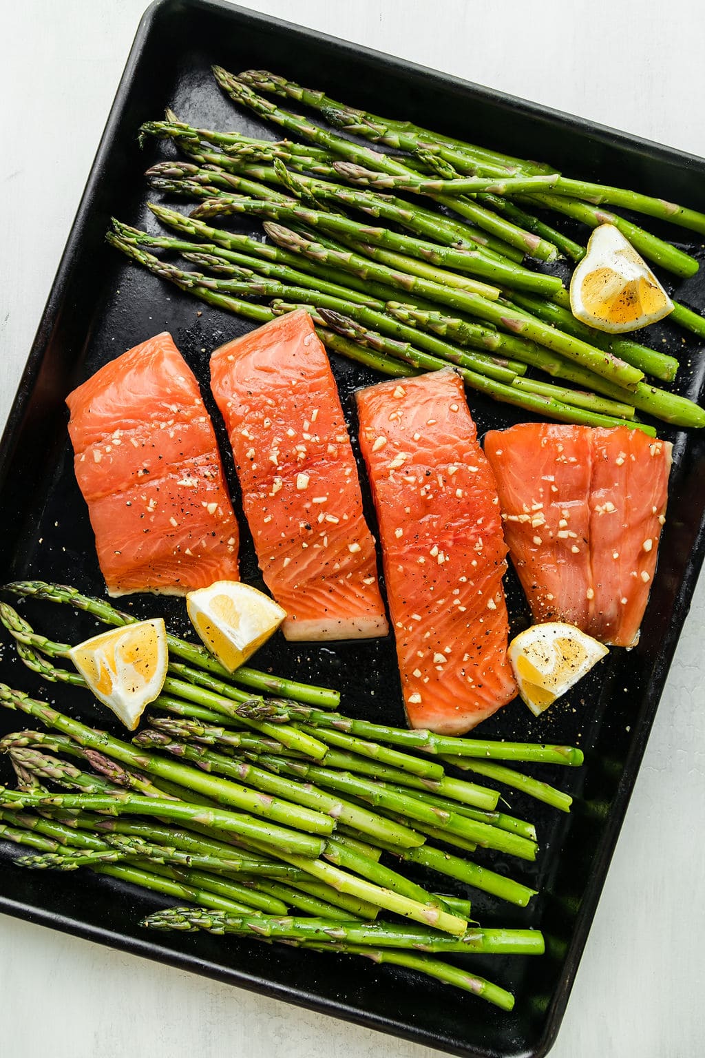 Sheet pan filled with salmon filets coated in honey garlic sauce with fresh asparagus on both side of sheet pan