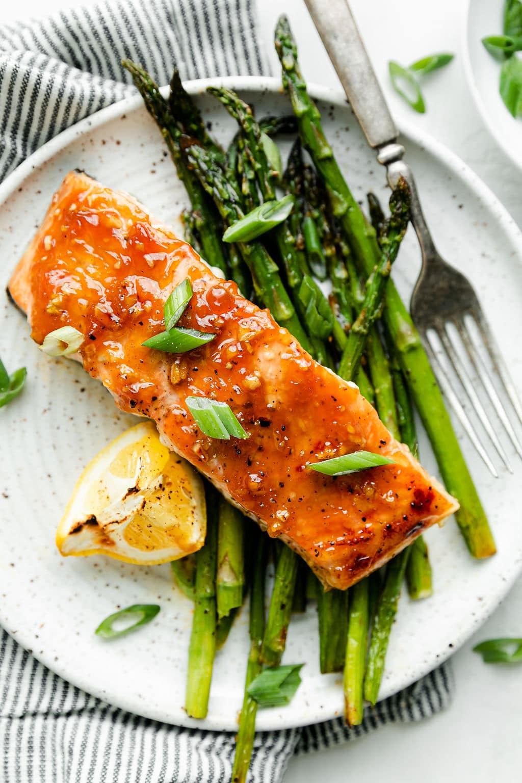 Overhead view honey glazed salmon filet on stone plate with roasted asparagus and lemon wedge.
