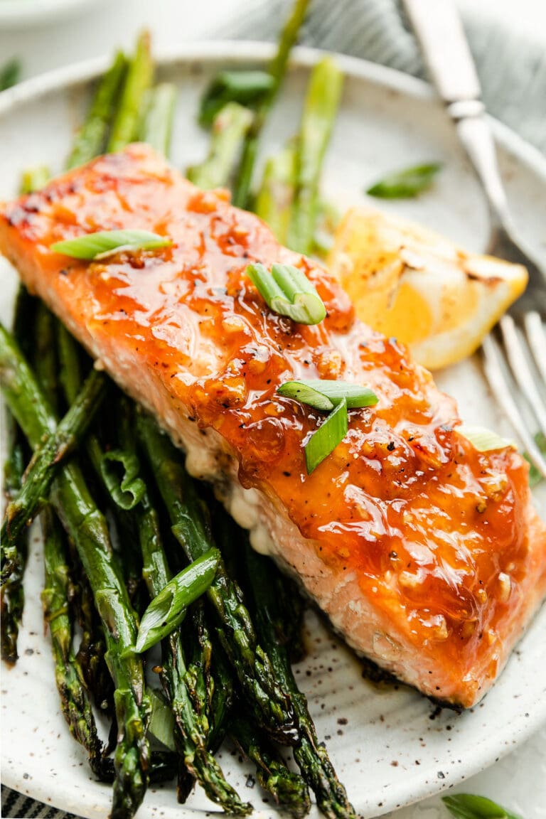 Sheet pan honey glazed salmon with asparagus on stone plate with lemon wedge.