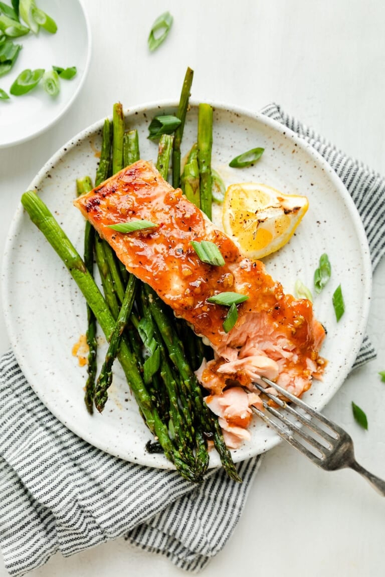 Overhead view of a plate of sheet pan honey glazed salmon with asparagus topped with green onions and garnished with a lemon wedge.