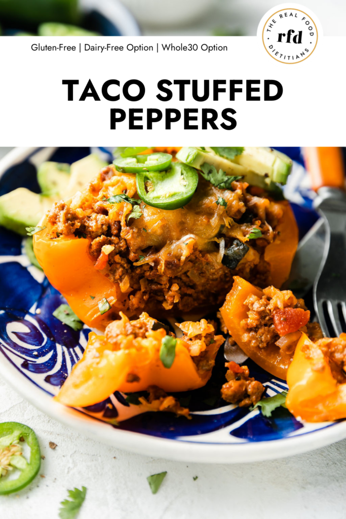 Taco stuffed pepper on blue plate, topped with cheddar cheese, avocado and jalapeño slices.