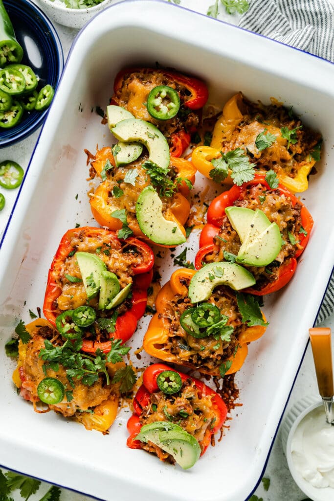 An overhead view of stuffed peppers fresh out of the oven and topped with avocado, jalapeno, and cilantro.