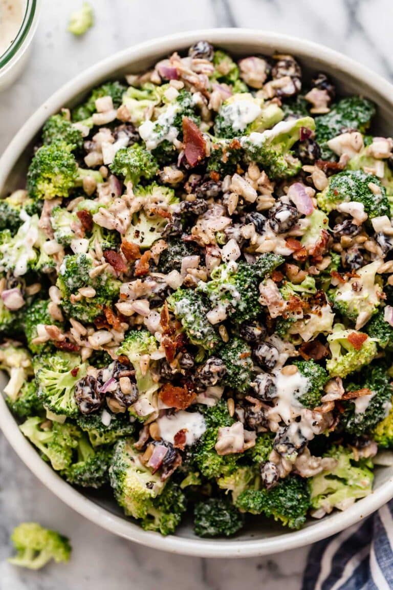 Overhead view of a serving bowl of cream broccoli salad topped with crisp bacon and raisins.