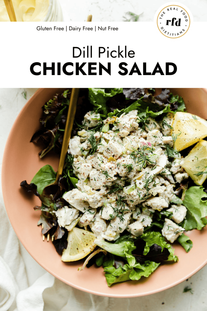 Overhead view dill pickle chicken salad served over mixed greens topped with fresh dill and lemon wedges.