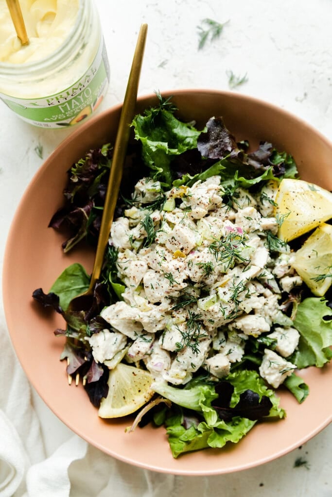 Dill pickle chicken salad served over mixed greens in pink bowl with gold cutlery.