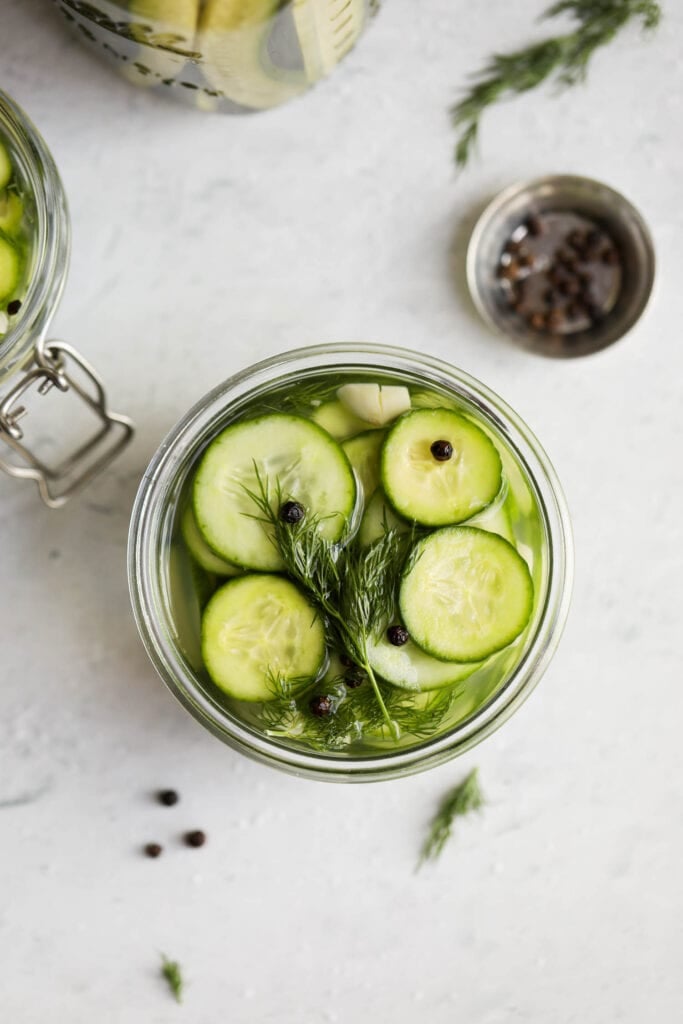 An overhead view of fast and easy refrigerator pickle chips, with fresh dill garlic and peppercorns.