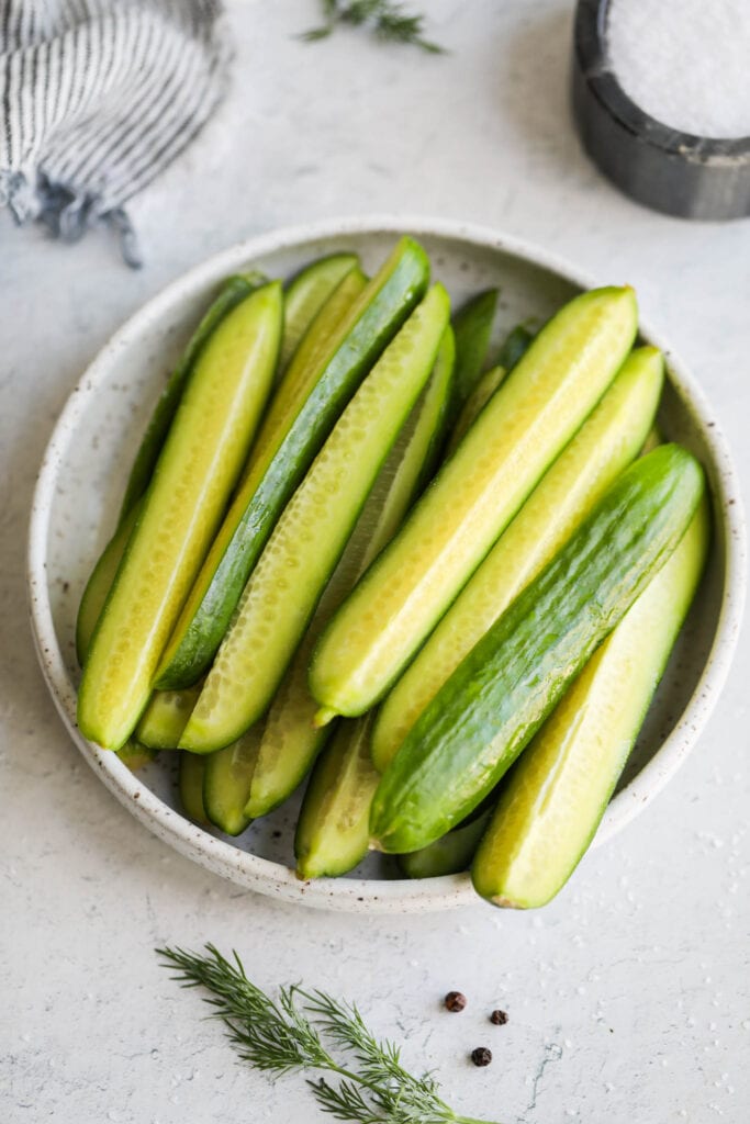 Prepped cucumbers sliced into spears on a plate. 