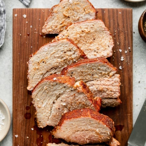 Overhead view grilled pork loin with easy rub cut into thick slices on wooden cutting board.