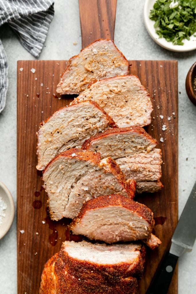 Overhead view grilled pork loin cut into thick slices on wooden cutting board.