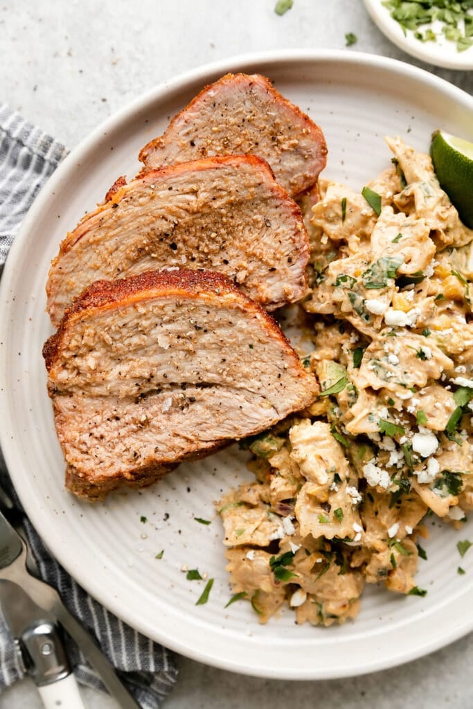 Grilled pork loin slices on stone plate with side of Mexican street corn pasta salad.