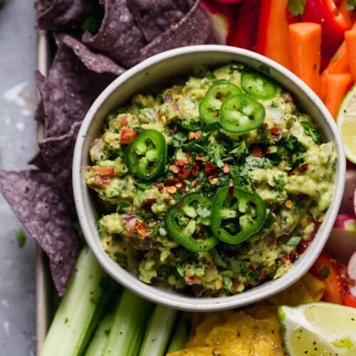 An overhead view of homemade guacamole with fresh sliced jalapenos and served with fresh veggies and tortilla chips.