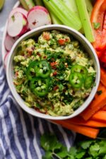 A bowl of fresh and easy guacamole served with sliced radishes, celery, bell peppers, and carrots. 