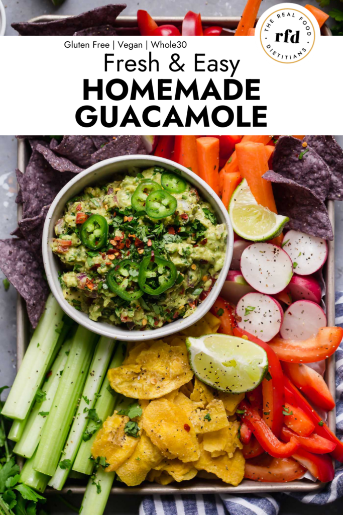 Overhead view homemade chunky guacamole in white bowl on tray with colorful veggies and blue chips