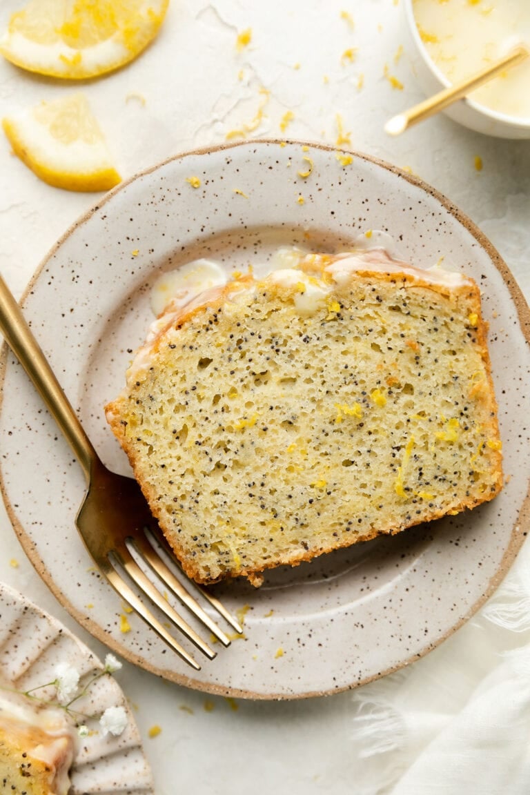 A slice of fresh lemon poppy seed bread on a white plate drizzled with icing. 