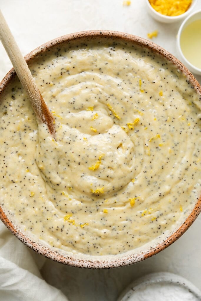 Lemon poppy seed bread batter being stirred in brown bowl with wooden spoon.