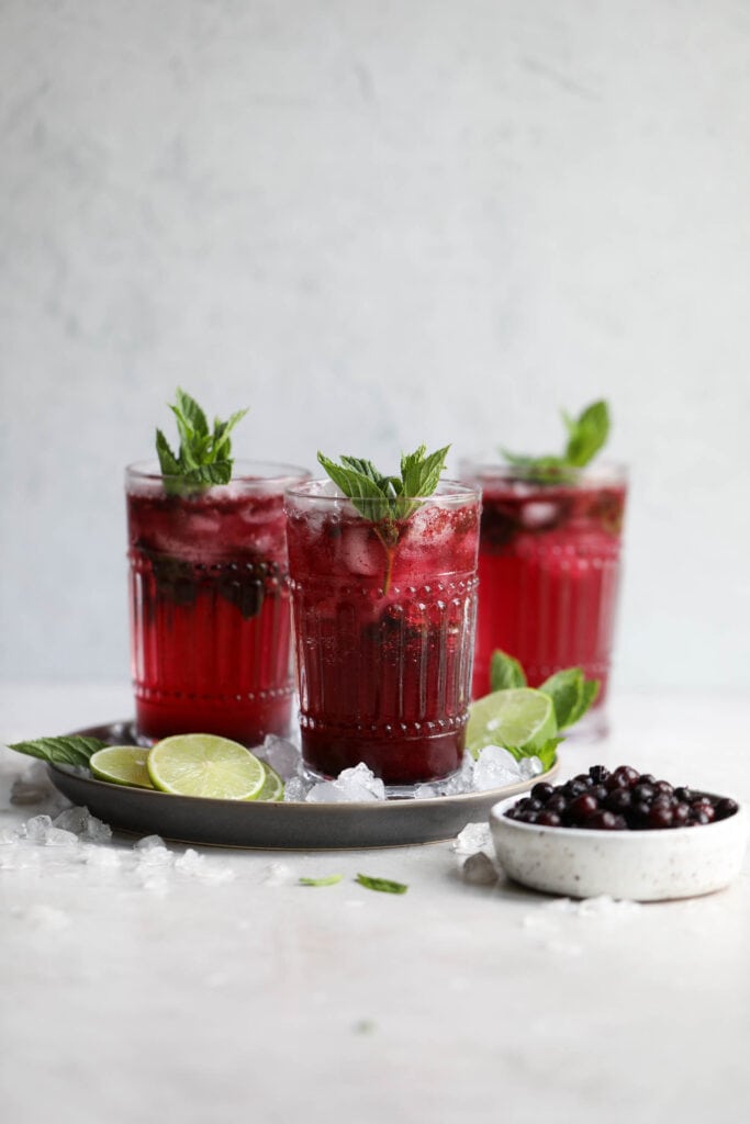 Three tall glasses blueberry mojitos on silver tray, topped with fresh mint sprigs.