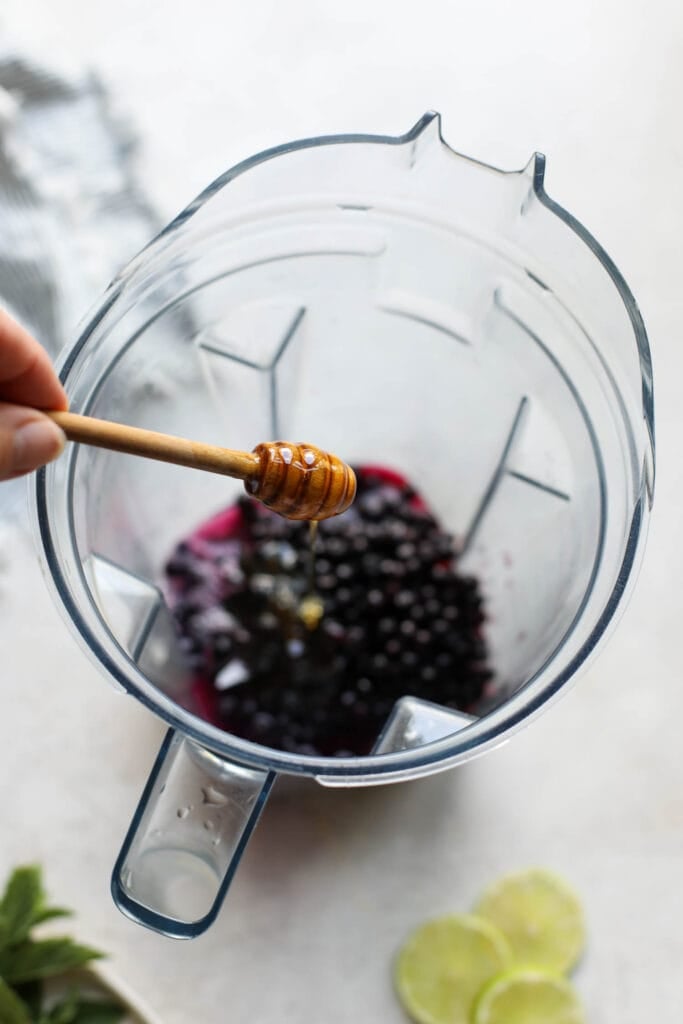 Honey being drizzled into blender cup with wild blueberries in bottom 