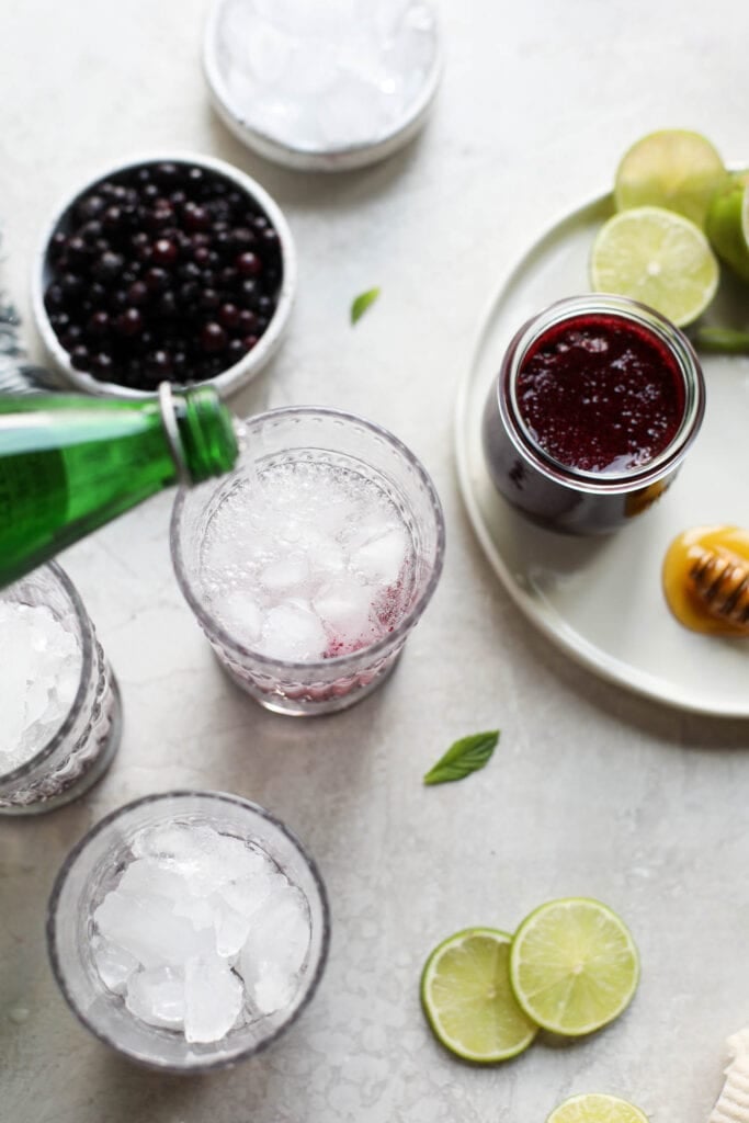 Sparkling water being poured into tall glass for blueberry mojito