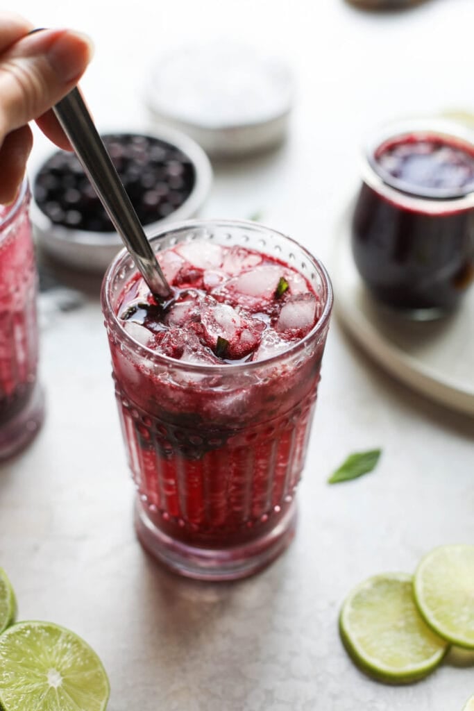 A spoon stirring up a blueberry mojito cocktail in tall glass cup