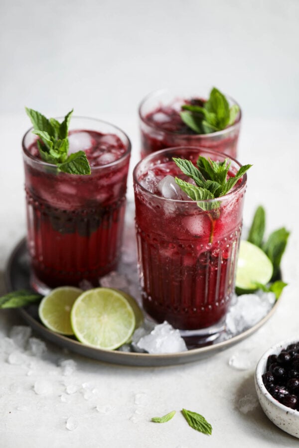 Three tall glasses blueberry mojito on silver tray
