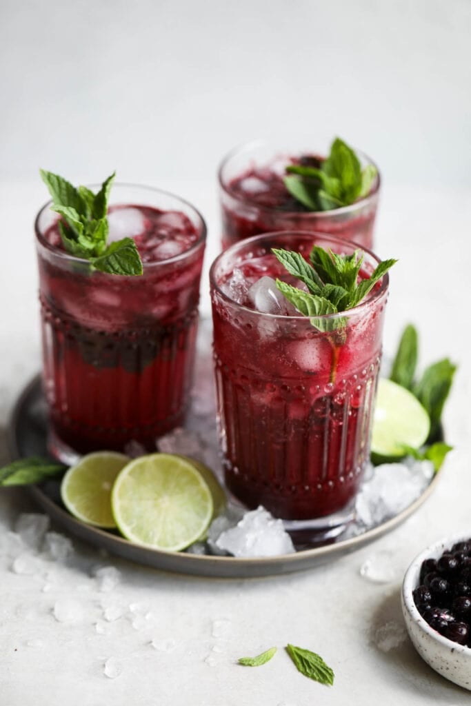 Three tall glasses filled with blueberry mojitos, sprigs of mint in each glass.