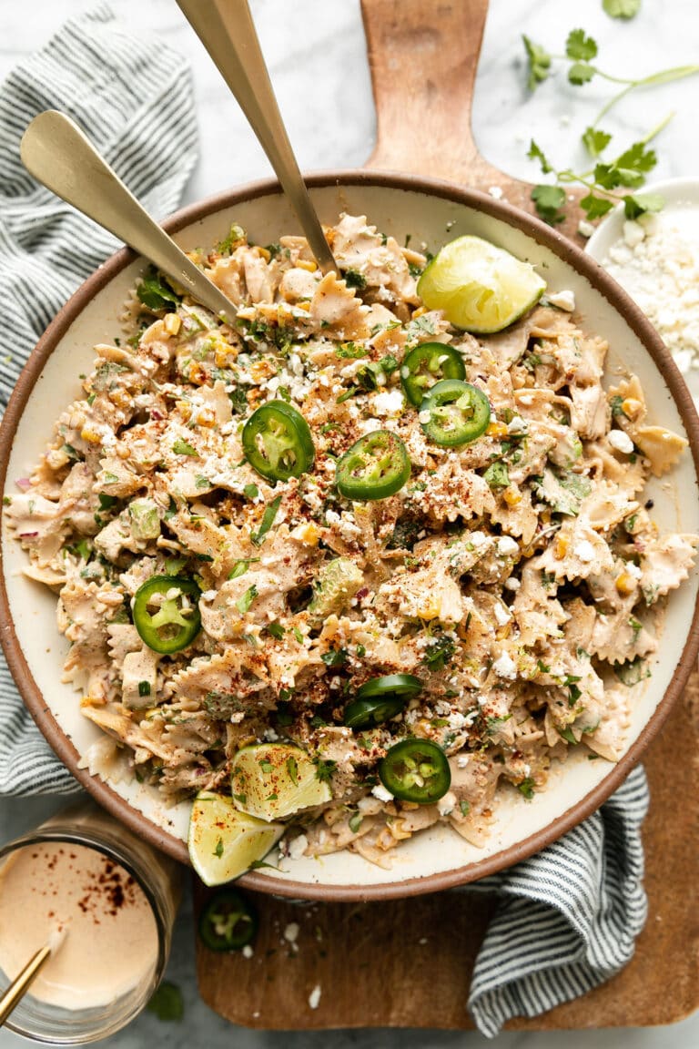 Mexican Street Corn Pasta Salad in stone bowl topped with limes and jalapeno slices.