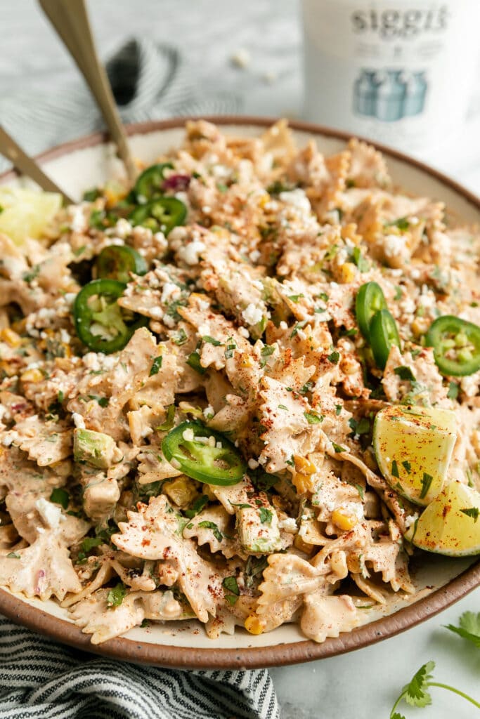 Side view Mexican Street Corn Pasta Salad in stone bowl topped with jalapeño slices and lime wedges.