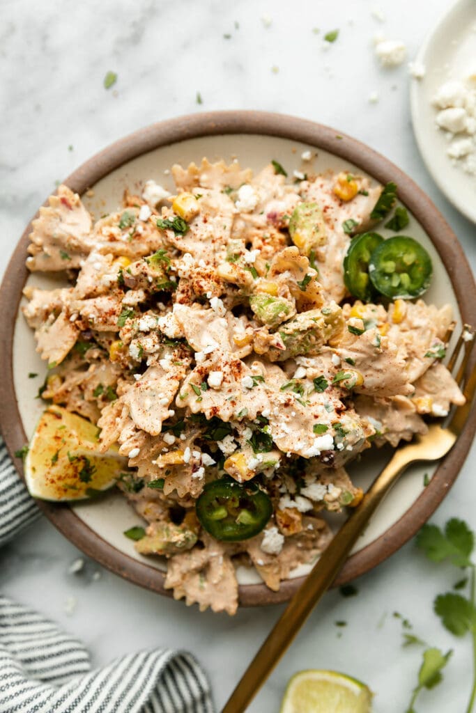 Mexican Street Corn Pasta Salad coated in sauce and crumbled cheese in stone bowl