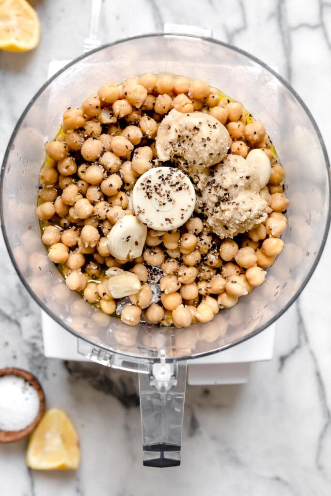 An overhead view of chickpeas and other ingredients for hummus in food processor