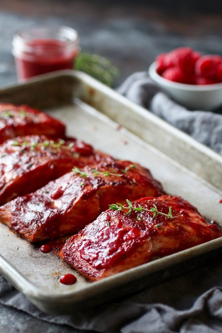 Close up view of a sheet pan of raspberry balsamic glazed salmon topped with fresh thyme. 
