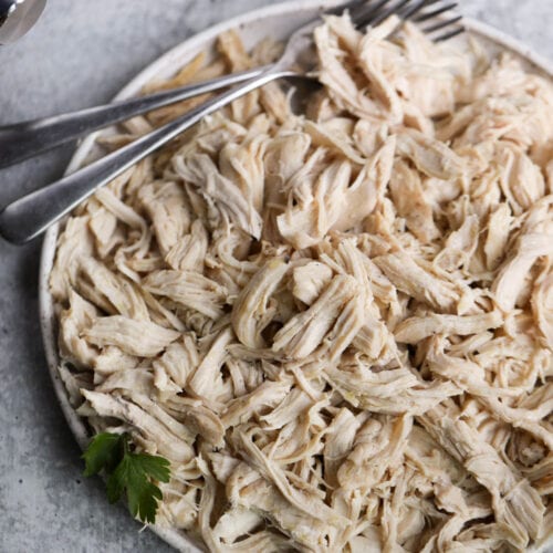 Stone plate filled with instant pot shredded chicken, two forks on chicken shreds.