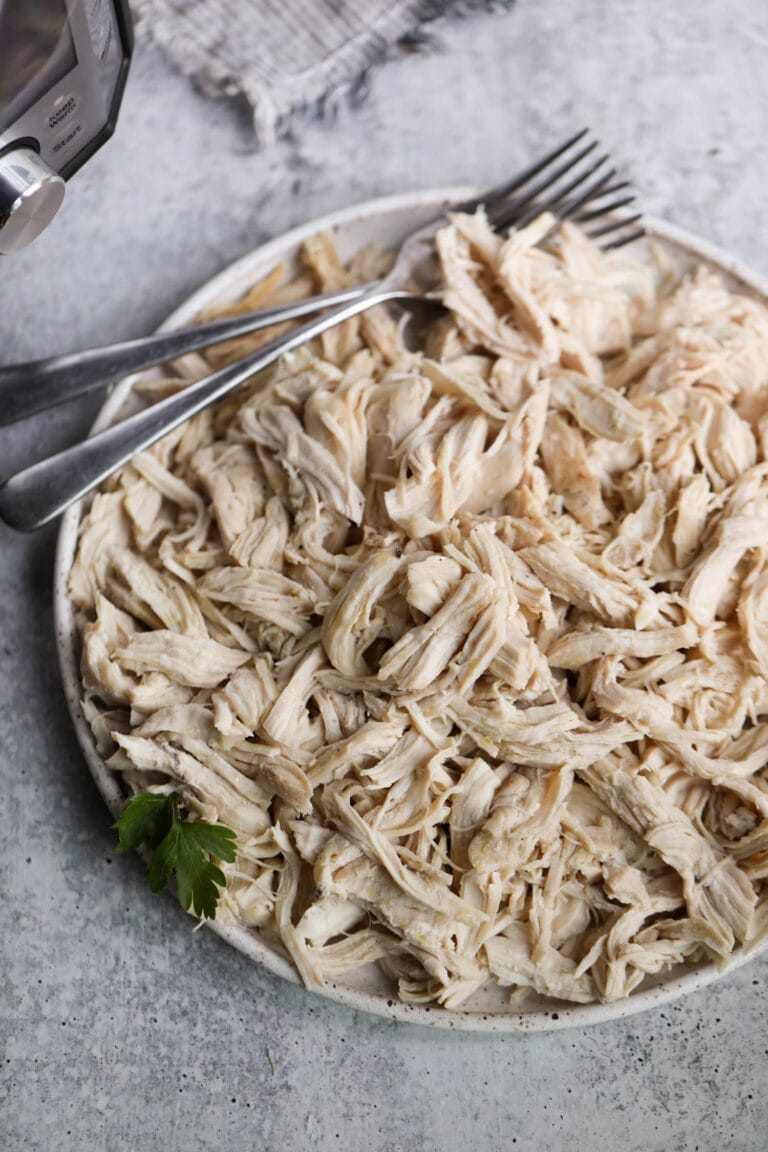 Stone plate filled with instant pot shredded chicken, two forks on chicken shreds.