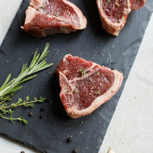 Overhead view raw lamb chops seasoned with salt and pepper with fresh herbs