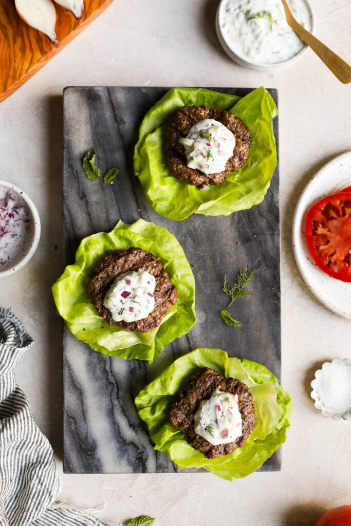 Grilled lamb burgers on lettuce wraps topped with tzatziki sauce.