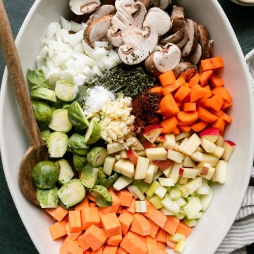 Overhead view white casserole dish filled with fresh cut vegetables and root vegetables