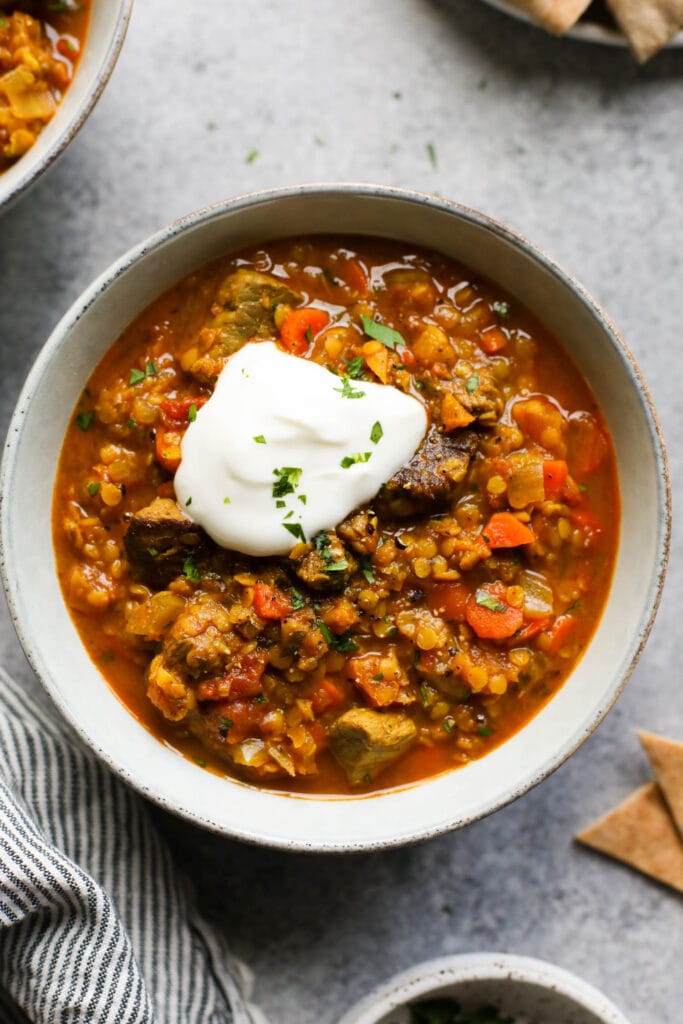 Overhead view stone bowl filled with beef and lentil stew topped with sour cream.