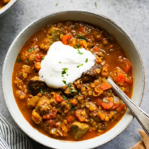 Overhead view stone bowl filled with beef and lentil stew topped with cream