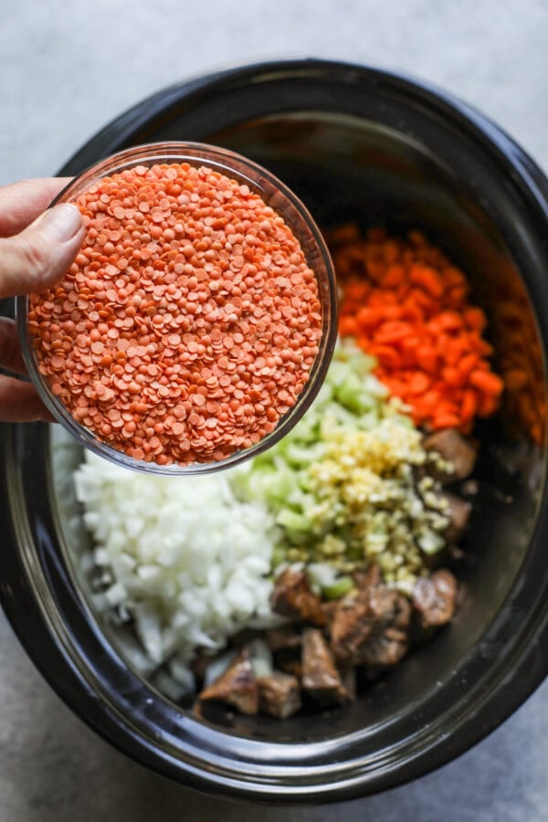 A small bowl of red lentils held over a crockpot with vegetables in it.